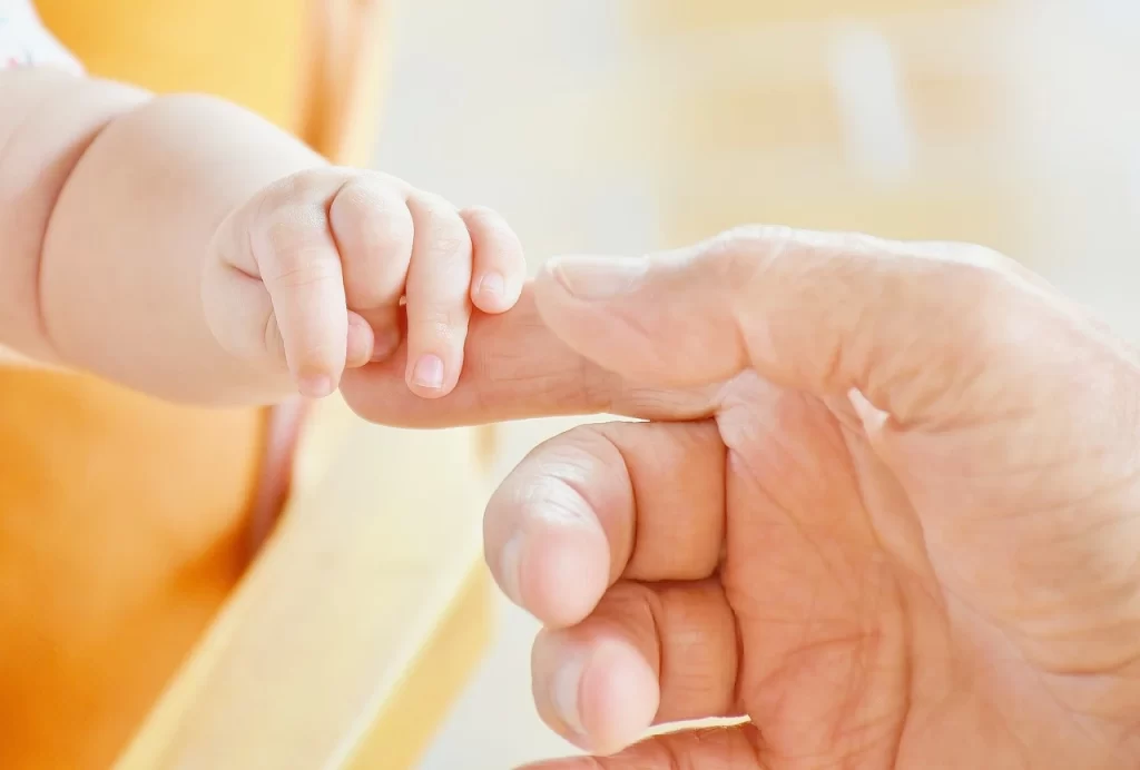 surrogate baby holding his legal parent's finger 